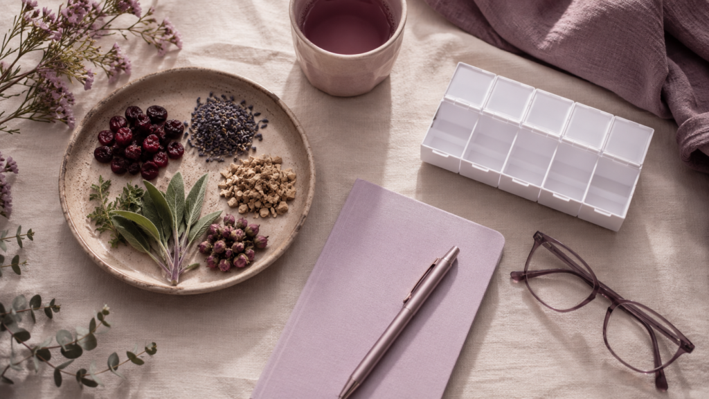 Overhead flatlay with herbal ingredients on one side, a pill organizer on the other, and a notebook between them